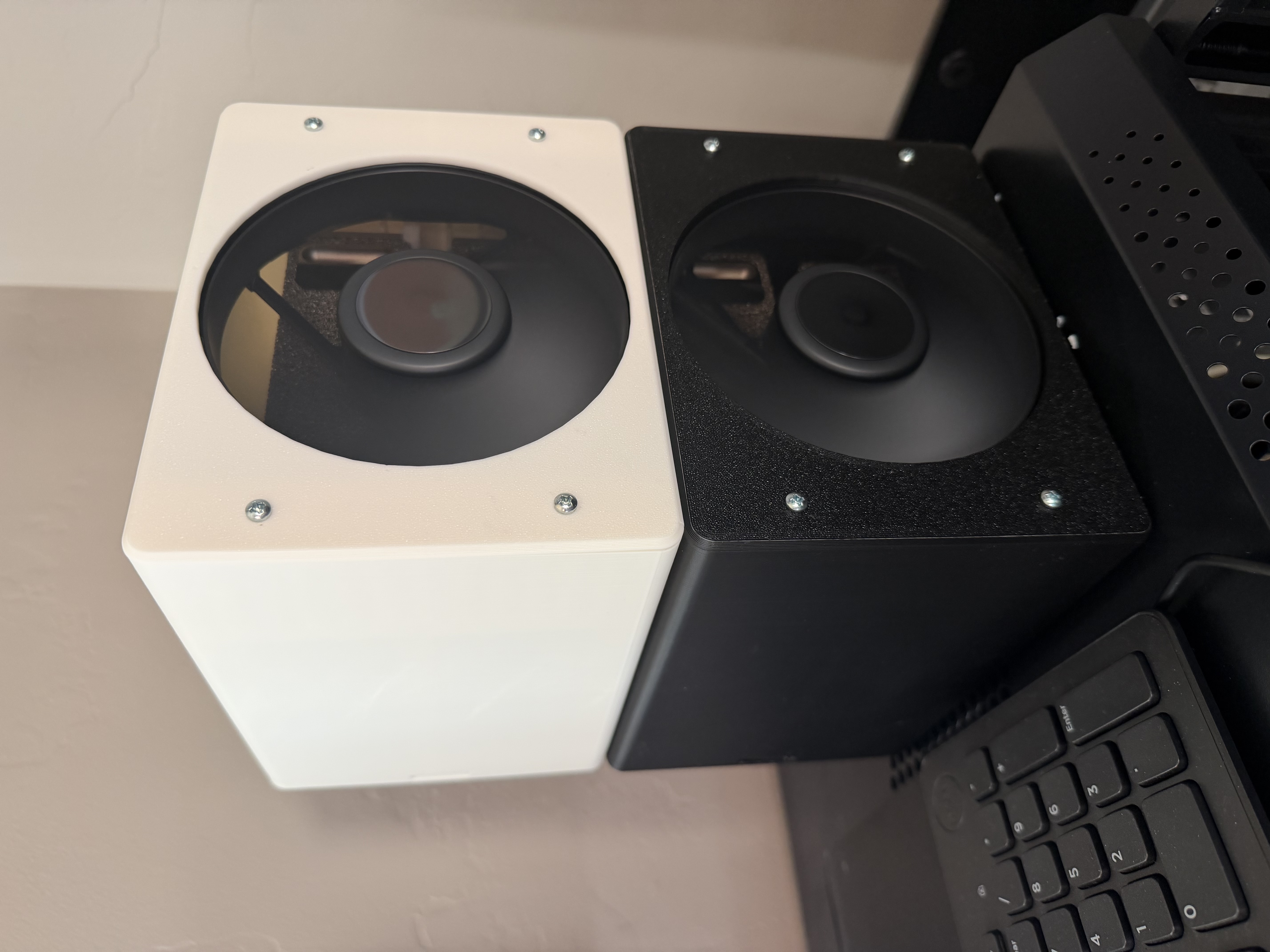 White and black printed cooling cases stacked on a rack, each with a large front fan and four bezel screws.
