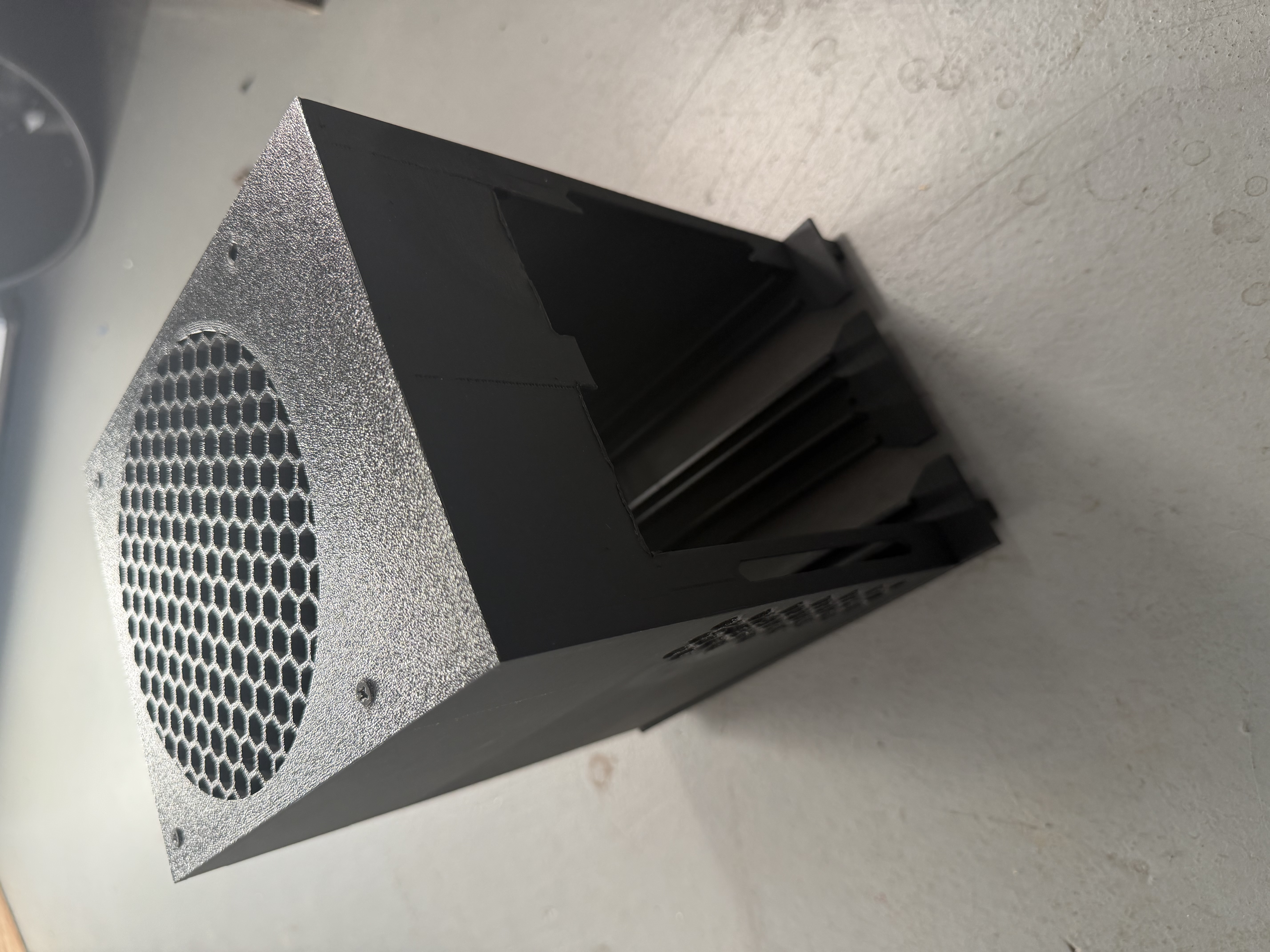 An upright black printed enclosure with a honeycomb top grille and an open side for the computers.